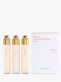 Three clear glass travel spray bottles with light pink liquid and gold-toned caps, next to a white box with gold and reddish