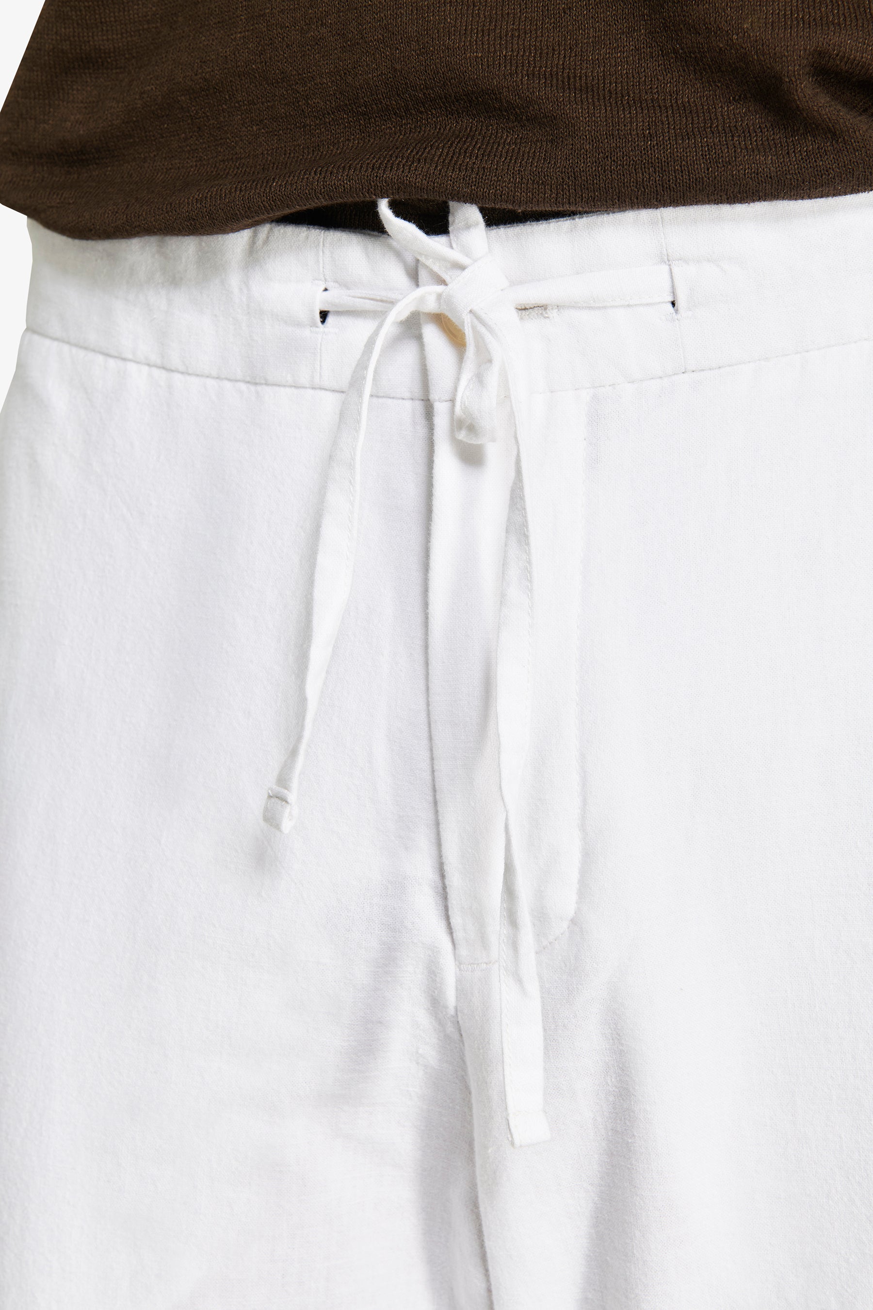 White linen blend trousers with a relaxed fit and a white drawstring tied in a bow at the front waist.