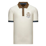 Off-white polo with brown collar, 3-button placket. Left chest: gold-toned eagle, brown/blue text. Short sleeves, dark blue c