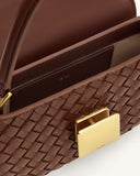 Brown hand-woven bag with a smooth round top handle. It has a gold-toned rectangular clasp and a brown interior flap.