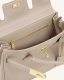 Light beige faux leather shoulder bag with gold-toned turn-lock closure, white contrast stitching, and an interior zip pocket
