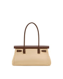 Light beige shoulder bag with a dark brown top flap. A single dark brown handle arches over the bag, attached by brown tabs w
