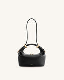 Black pebbled top-handle bag with two curved handles, each adorned with a gold-toned ring. Features a thin black strap and go