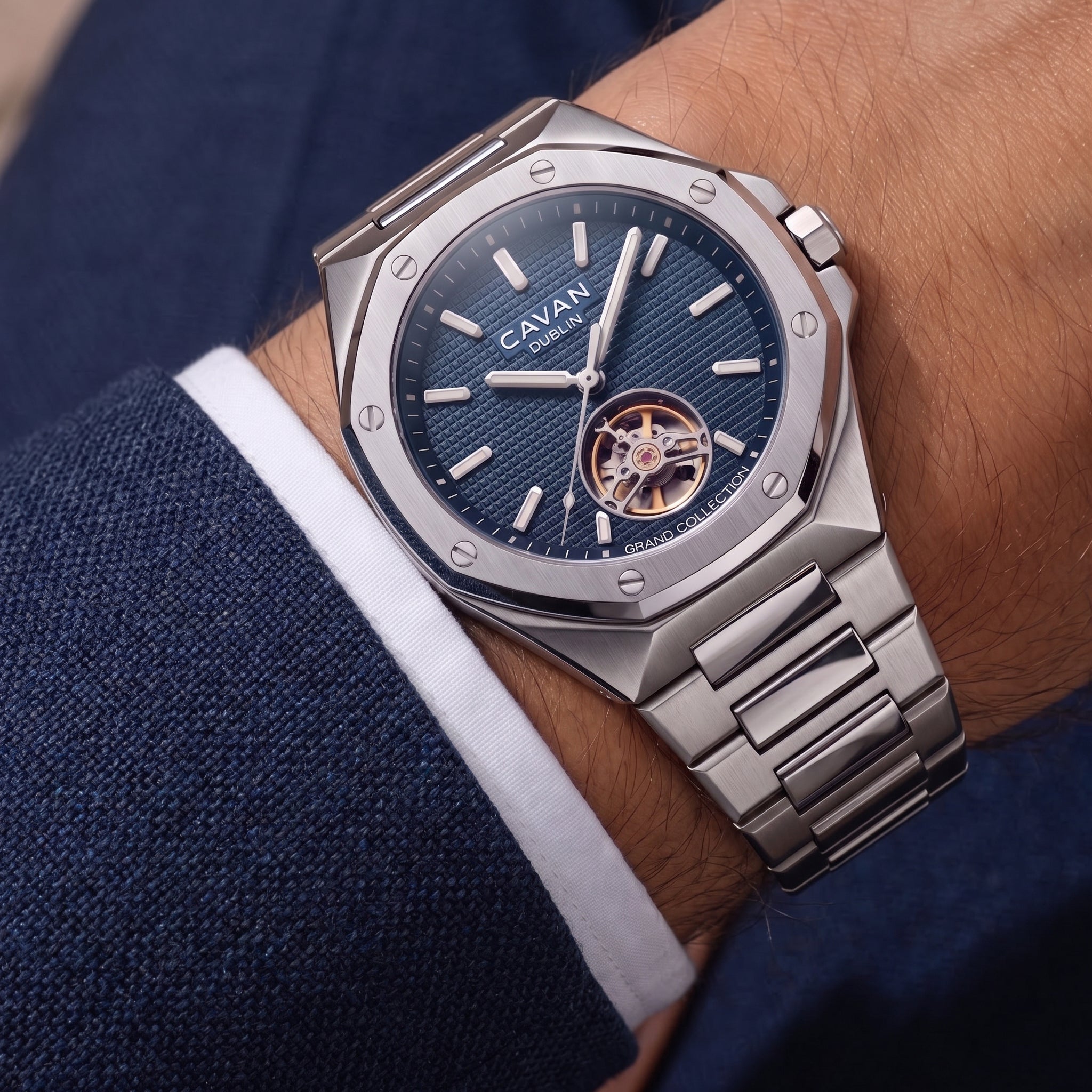 Silver-toned octagonal watch with blue textured dial, visible gold-toned gears, and a metal link bracelet.