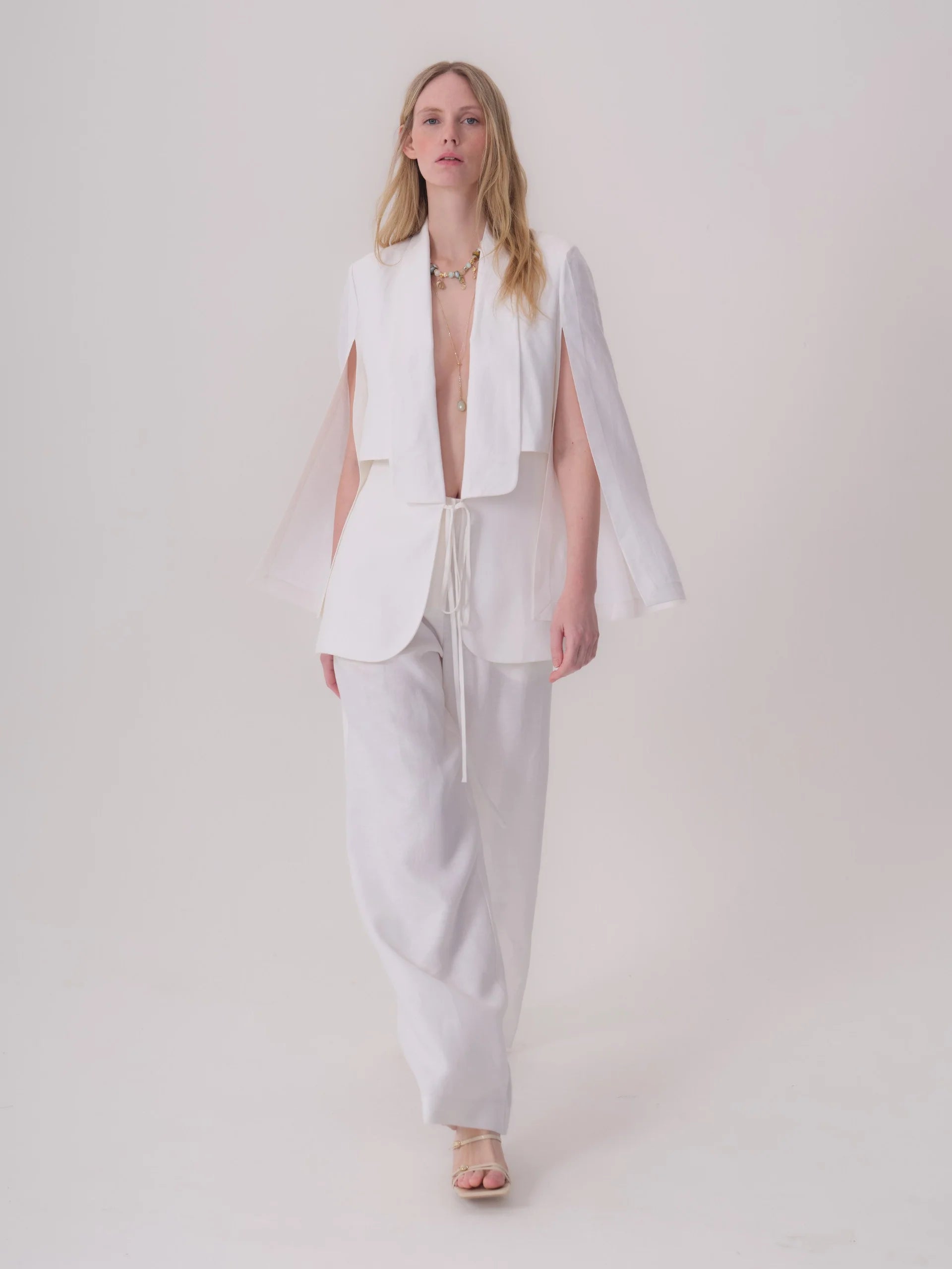 White linen-blend jacket with wide draped collar, open front, cape-style sleeves with slits, and a drawstring waist.