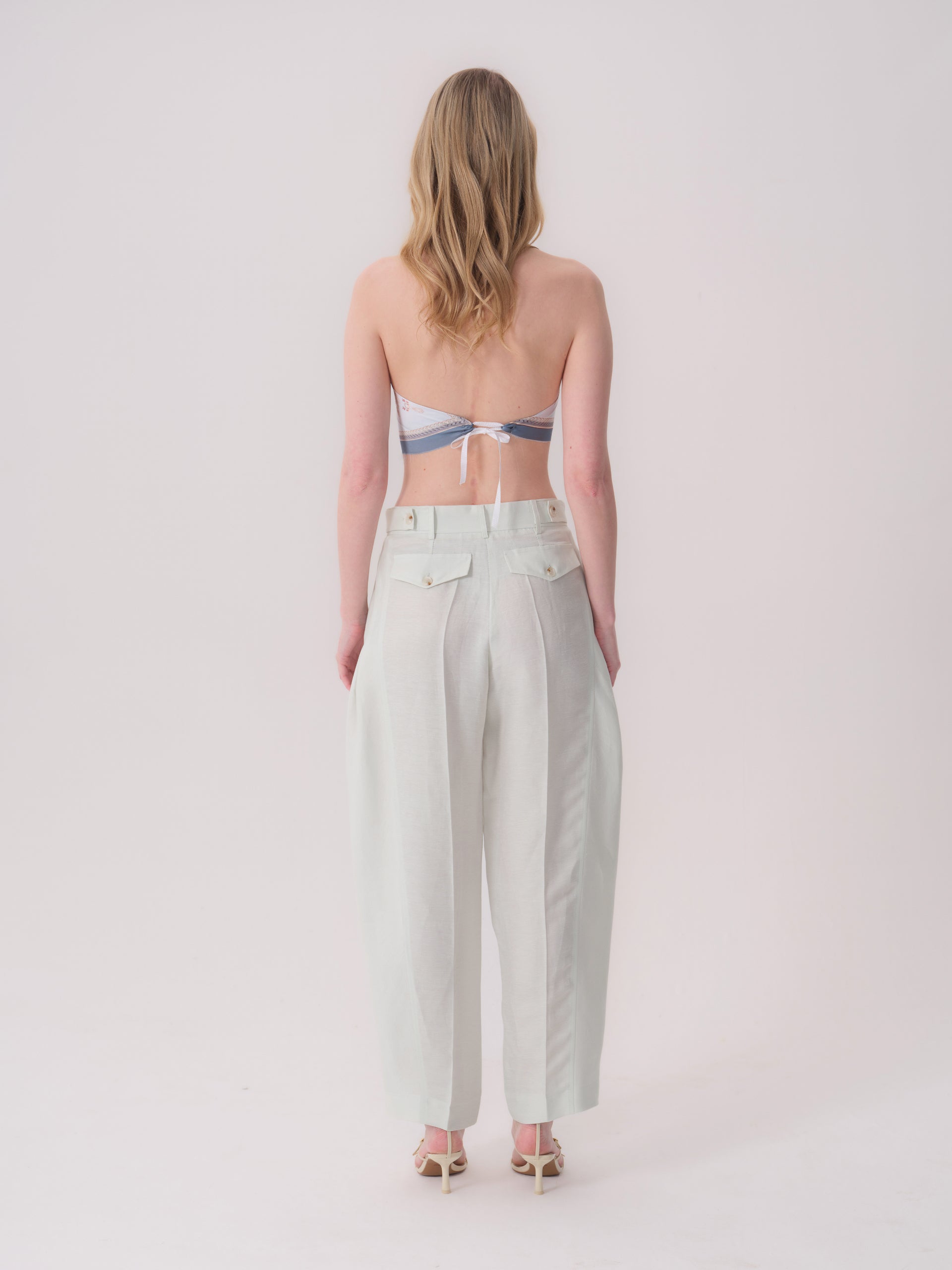 Mint green wide-leg trousers with two back flap pockets, each with a light button, and vertical seams down the back of each l
