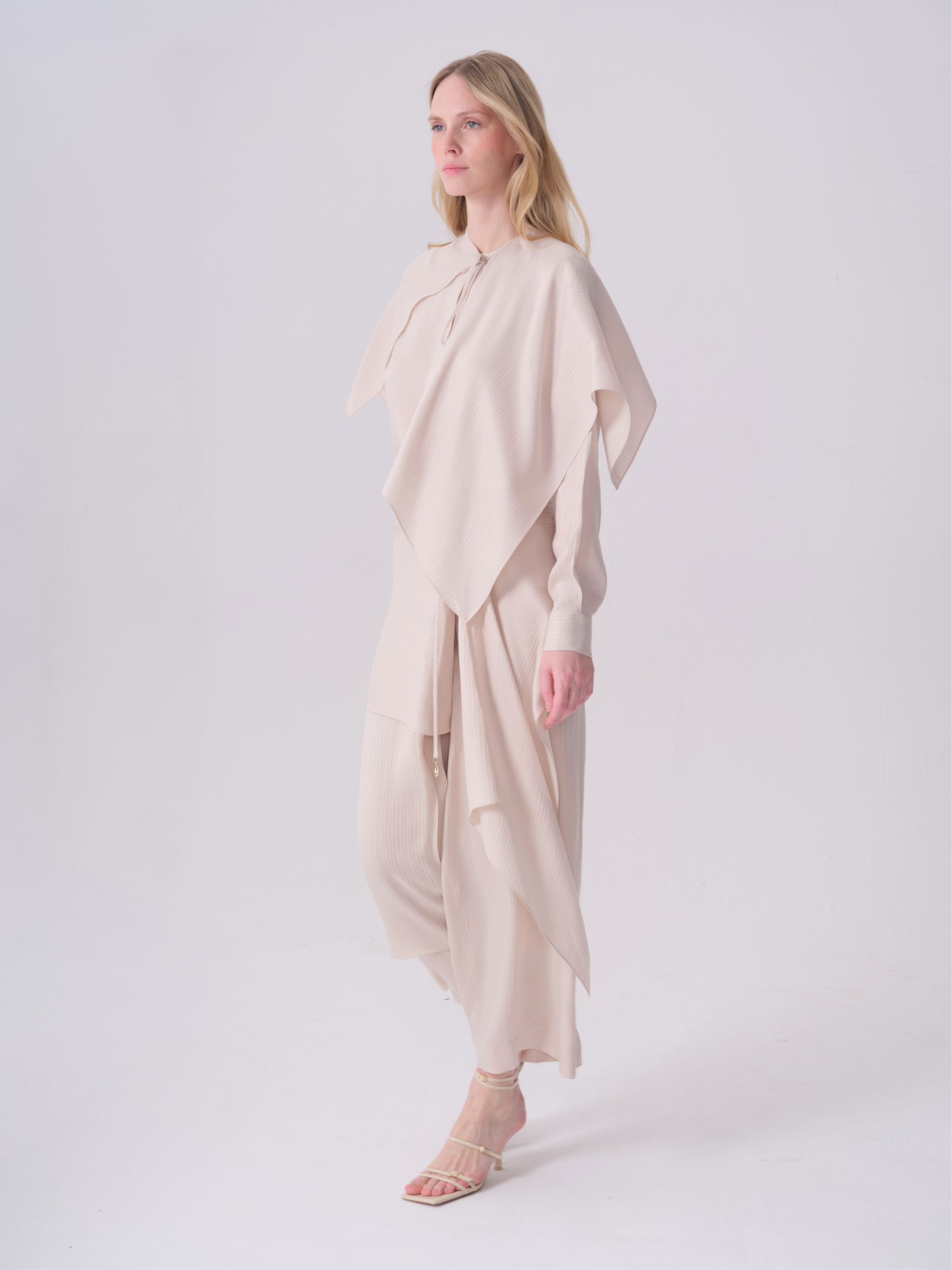 Light beige pleated trousers with a relaxed, wide-leg fit, cropped length, and a tie waist with a gold-toned bead.