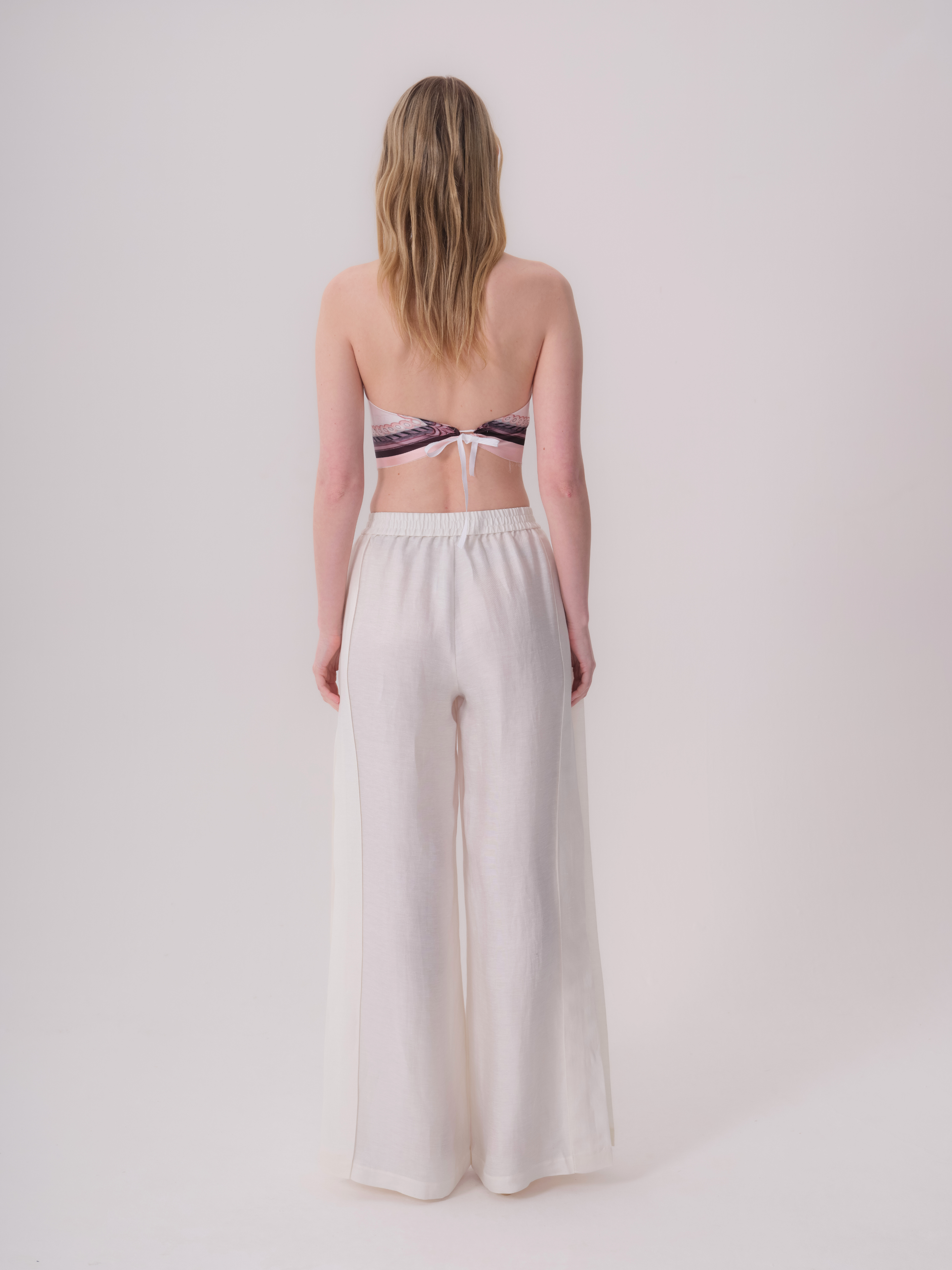 Ecru wide-leg trousers with an elasticated back waistband. Each leg has a vertical seam down the back, with a subtle side pan
