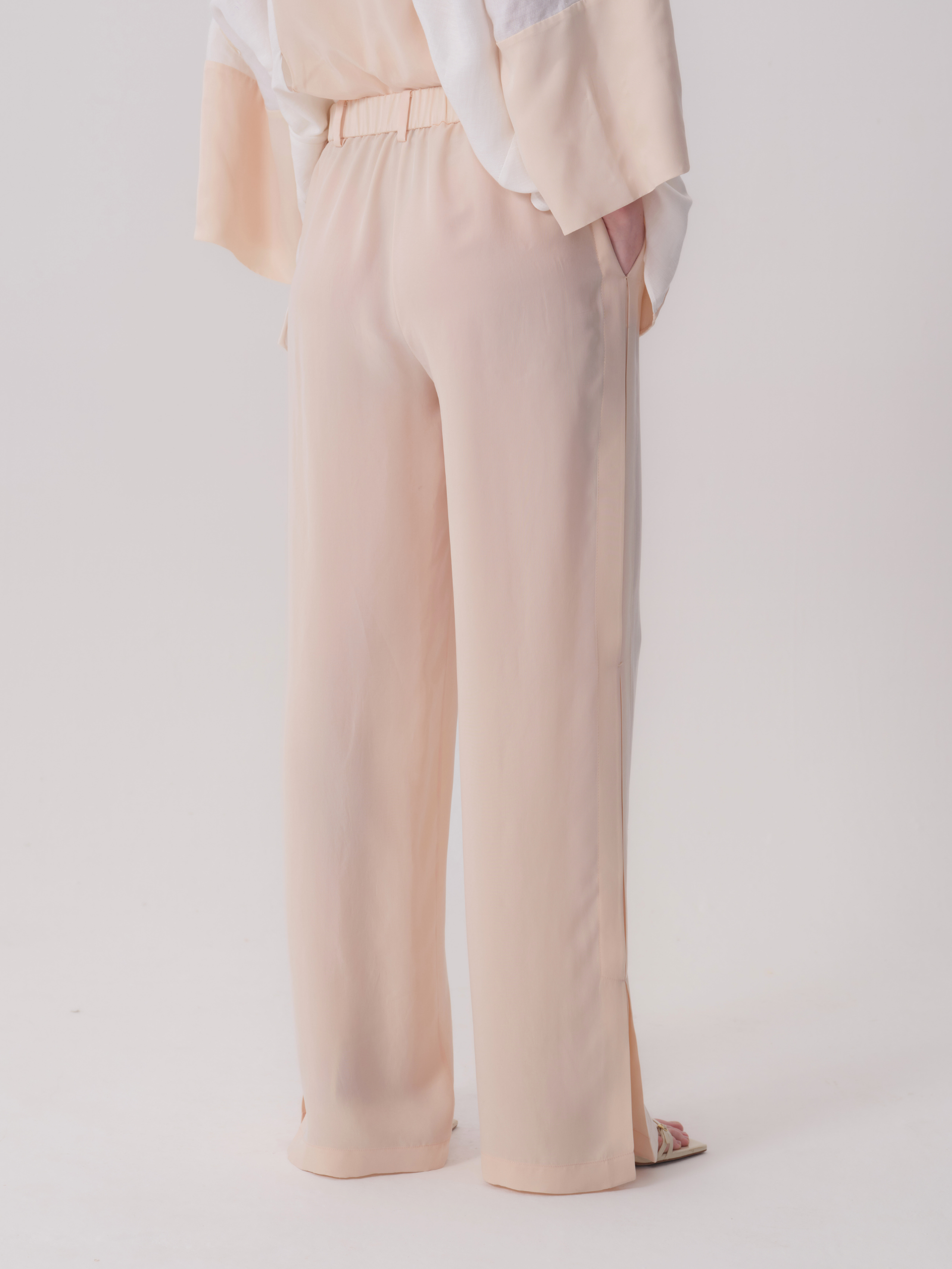 Cream wide-leg trousers with an elasticated waistband, side pockets, and ankle slits on both outer legs.