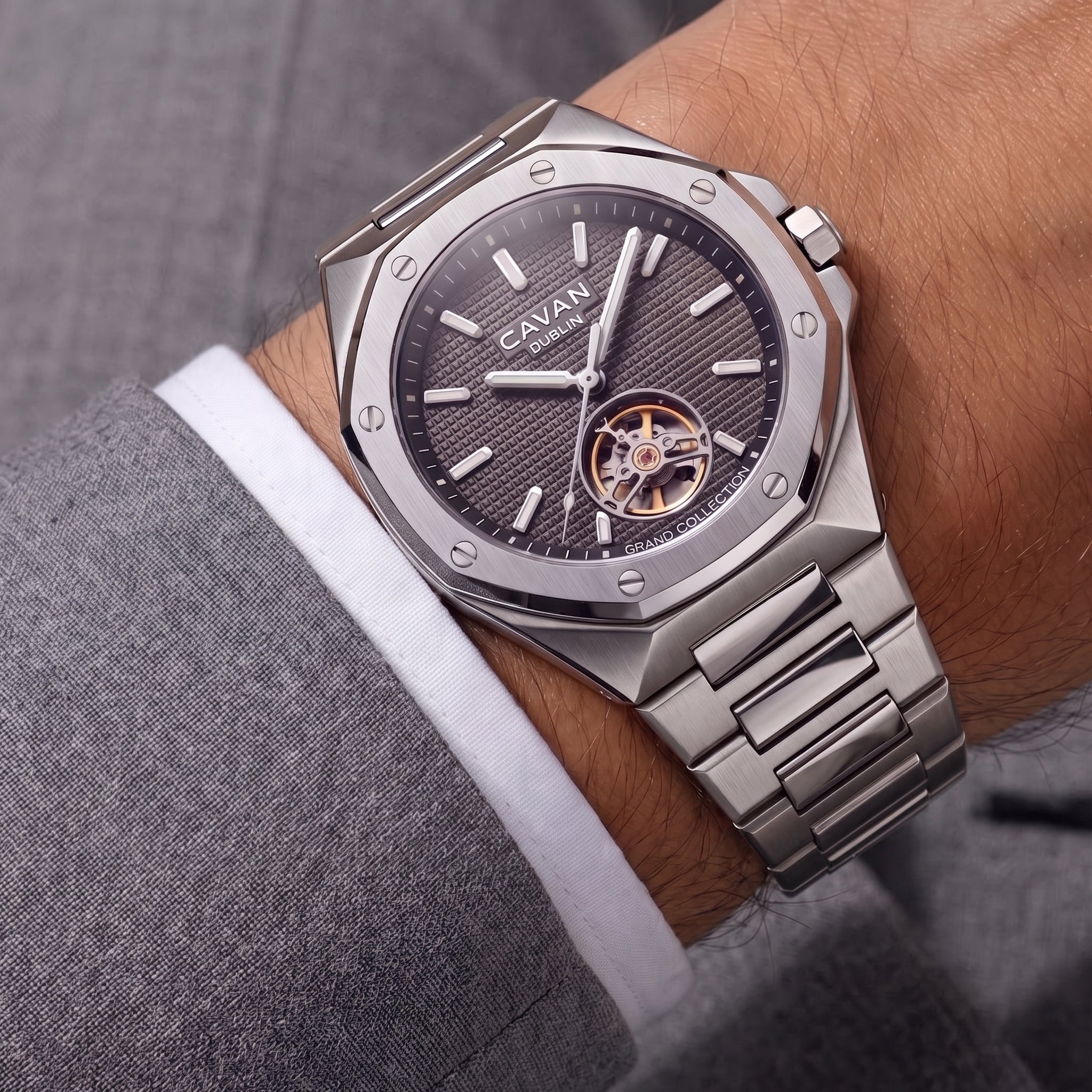 Silver-toned octagonal watch with a dark gray textured dial, visible gold-toned gears at 6 o'clock, and an integrated metal b