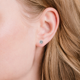 A single round, clear, faceted stud earring in a silver-toned four-prong setting.
