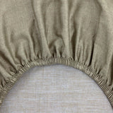 Beige bedding fabric with a subtle speckled texture and an elasticized, gathered edge.