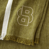 Jadeite green throw blanket with white vertical stripes, fringed edges, and a large embroidered light beige stylized 'B' logo