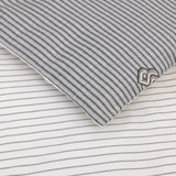 White bedding set. A pillow/duvet cover has thin dark gray stripes and a raised 'B' logo. The flat sheet has fine light gray