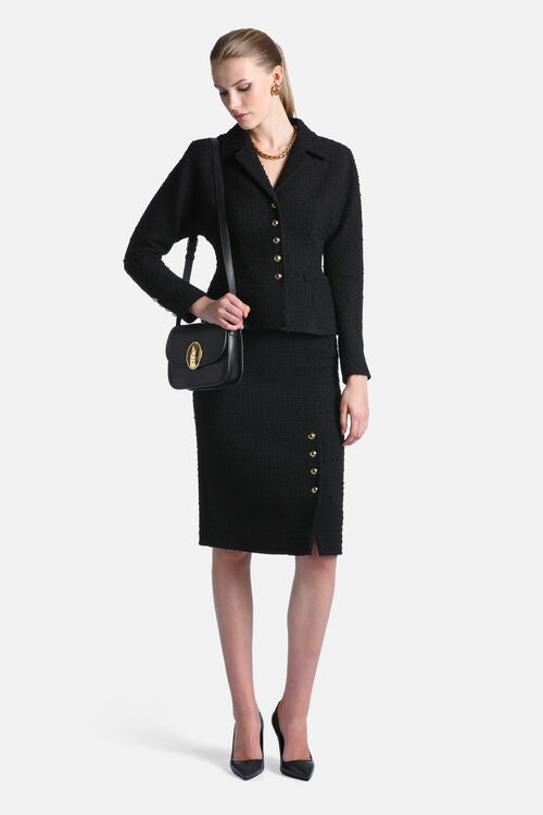 Black textured pencil skirt with a knee-length hem and a side slit, featuring four small gold-toned buttons.