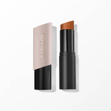 Lancome stick foundation with a matte black base and a pale pink angled cap, revealing a caramel-coloured foundation stick.