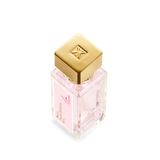 Clear square glass perfume bottle with light pink liquid and a pink label. It has a square gold-toned cap with an embossed lo