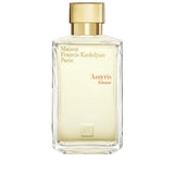 Clear glass perfume bottle with a light yellow liquid and a matte gold-toned rectangular cap, featuring brand text.