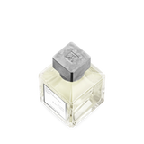 Square clear glass perfume bottle with light yellow liquid, a white label, and a textured silver-toned square cap with an emb