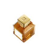 Square clear glass perfume bottle with amber liquid and a gold-toned square cap featuring an embossed logo. White label on fr