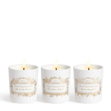 Set of three white Maison Francis Kurkdjian scented candles, each with a gold-toned botanical label, burning with a flame.