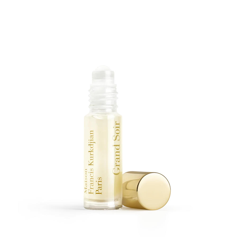 Clear glass roll-on perfume bottle with light yellow liquid, white applicator, and gold-toned text label. A gold-toned cylind