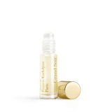 Clear glass roll-on perfume bottle with light yellow liquid, white applicator, and gold-toned text label. A gold-toned cylind