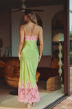 A woman wearing a lime green satin slip dress with pink floral lace trim at the back neckline and hem, shown from behind in a home interior setting.