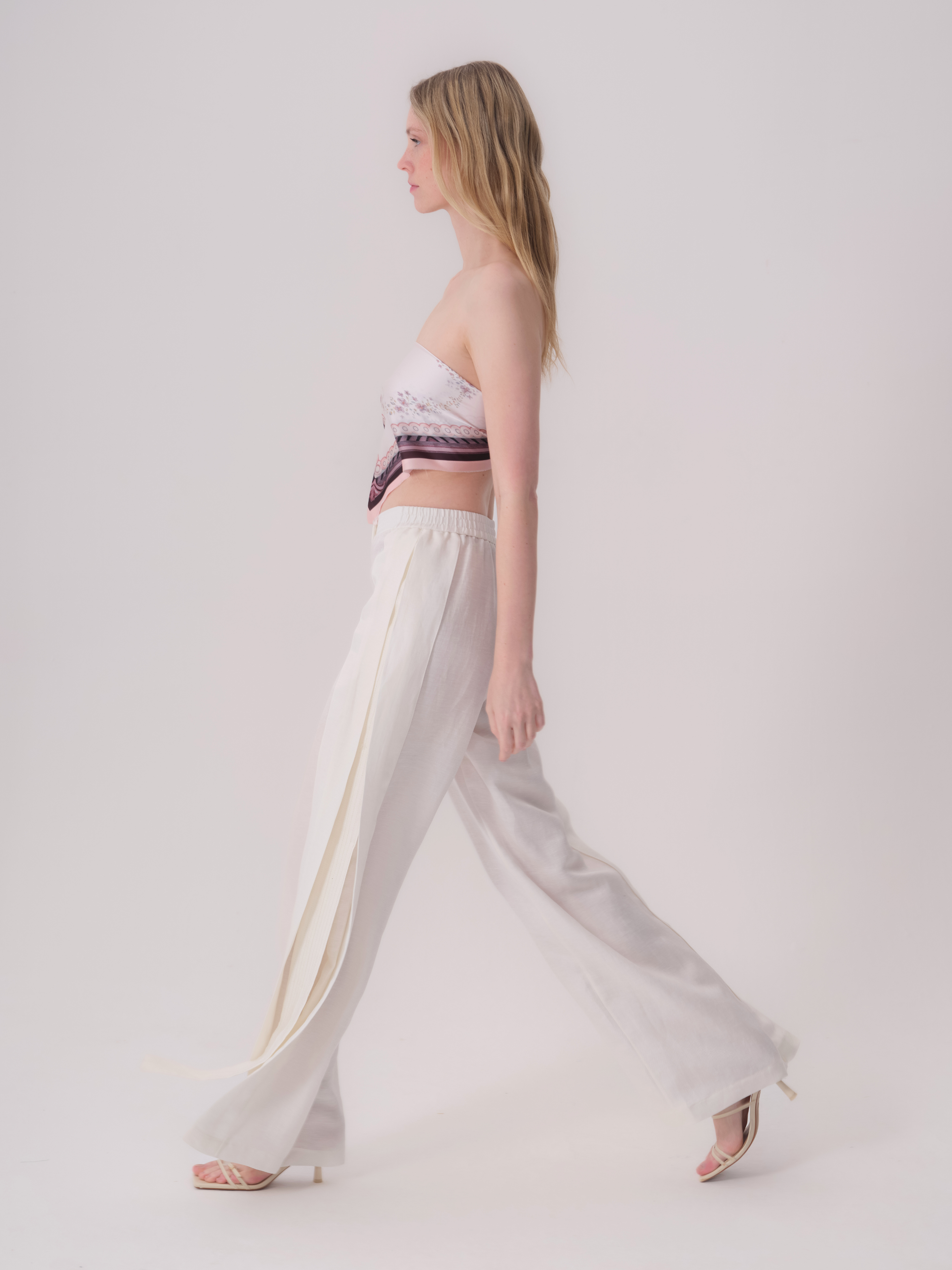Ecru wide-leg trousers with an elasticated waistband. The left leg features a vertical overlay panel creating a slit with a h