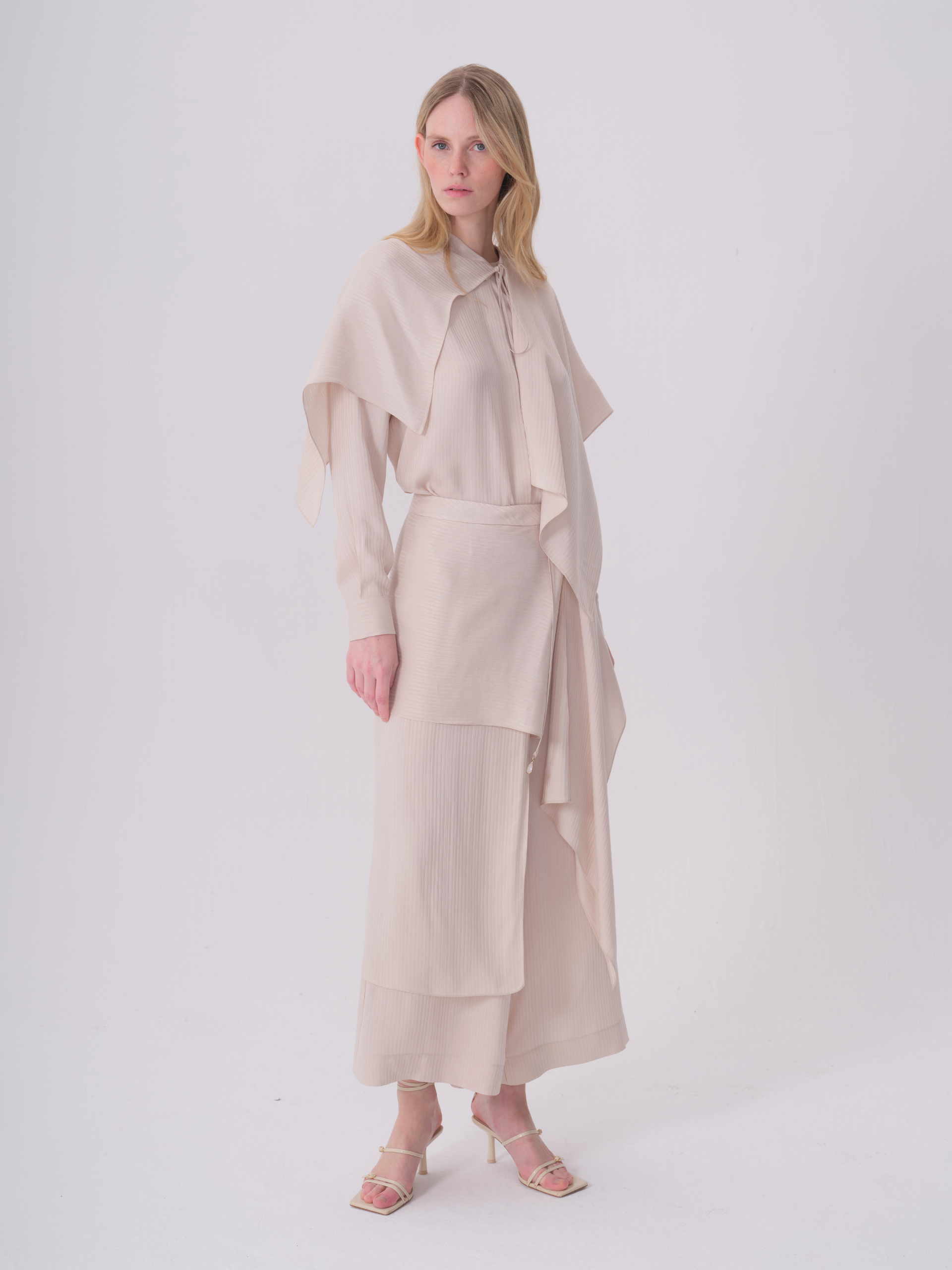 Off-white wide-leg trousers with a layered, wrap-style design. The top layer has fine vertical pleats.