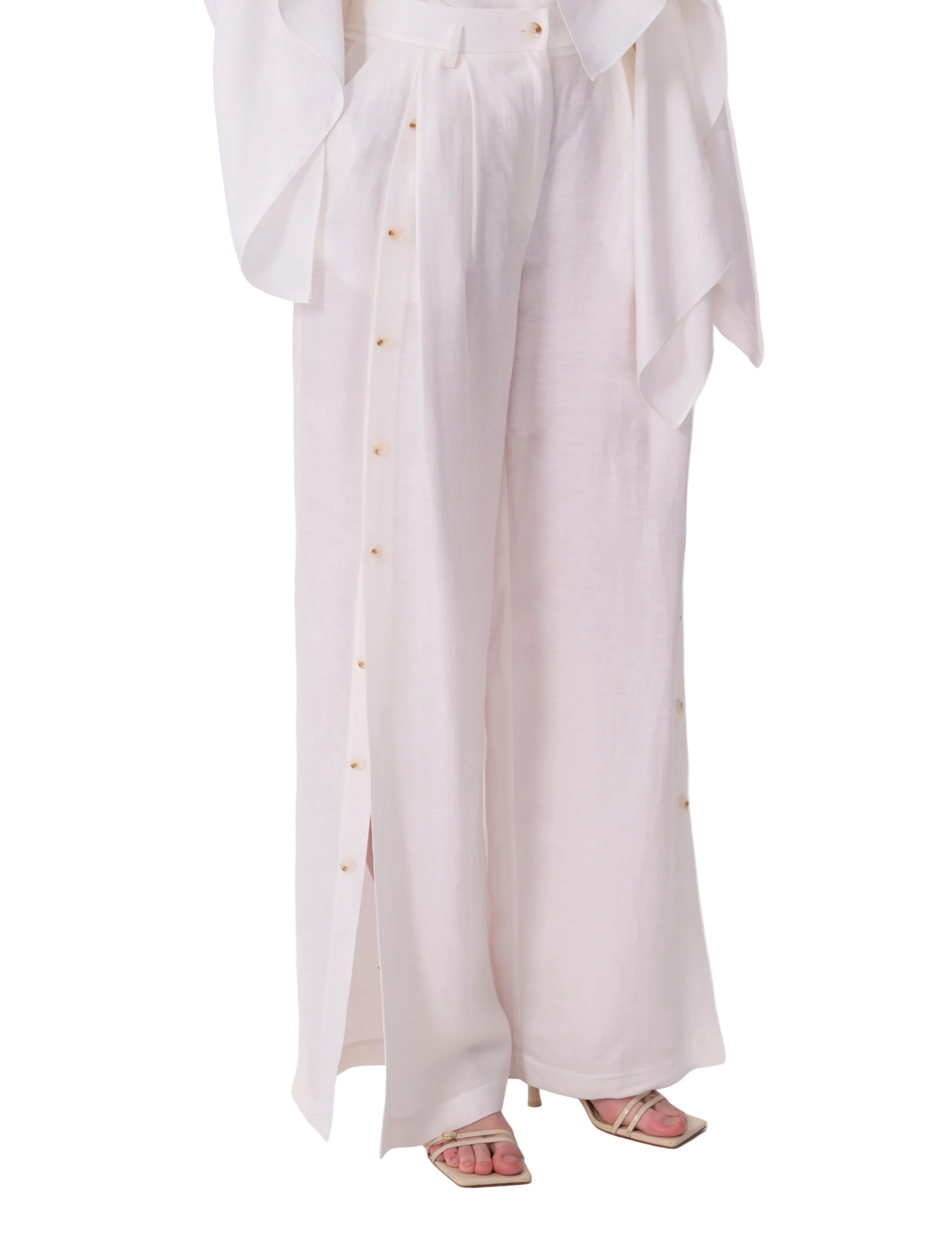 White wide-leg trousers with a high waist, front pleats, and full-length light brown buttons along the outer side seams.