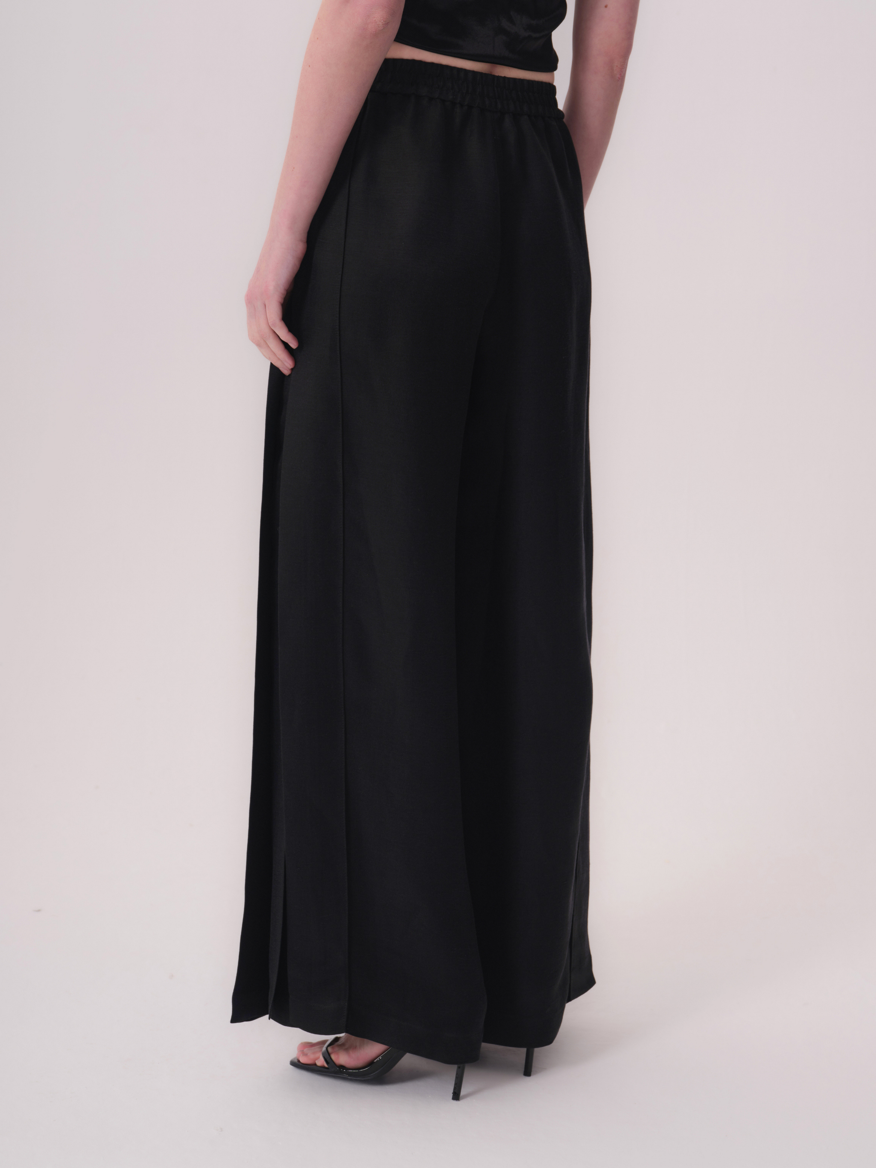 Black wide-leg trousers with an elasticated waistband, vertical front seams, and side slits on both legs.