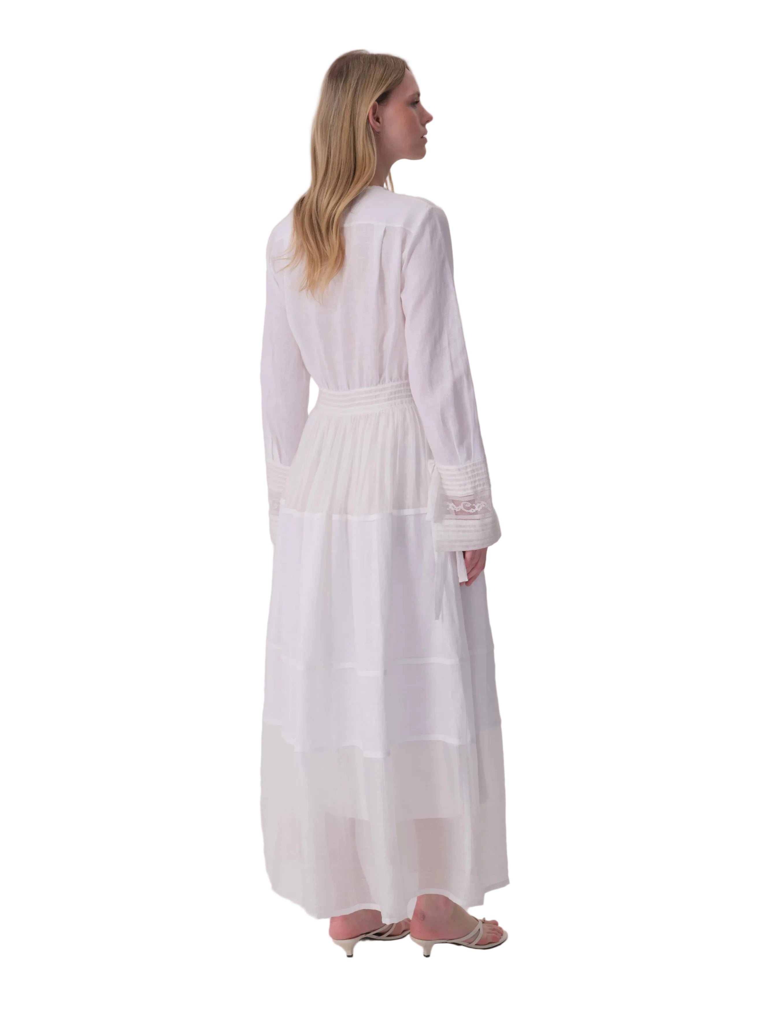White long-sleeved maxi dress with a shirt collar, smocked waist, and tiered skirt with sheer panels. Lace detail on cuffs.