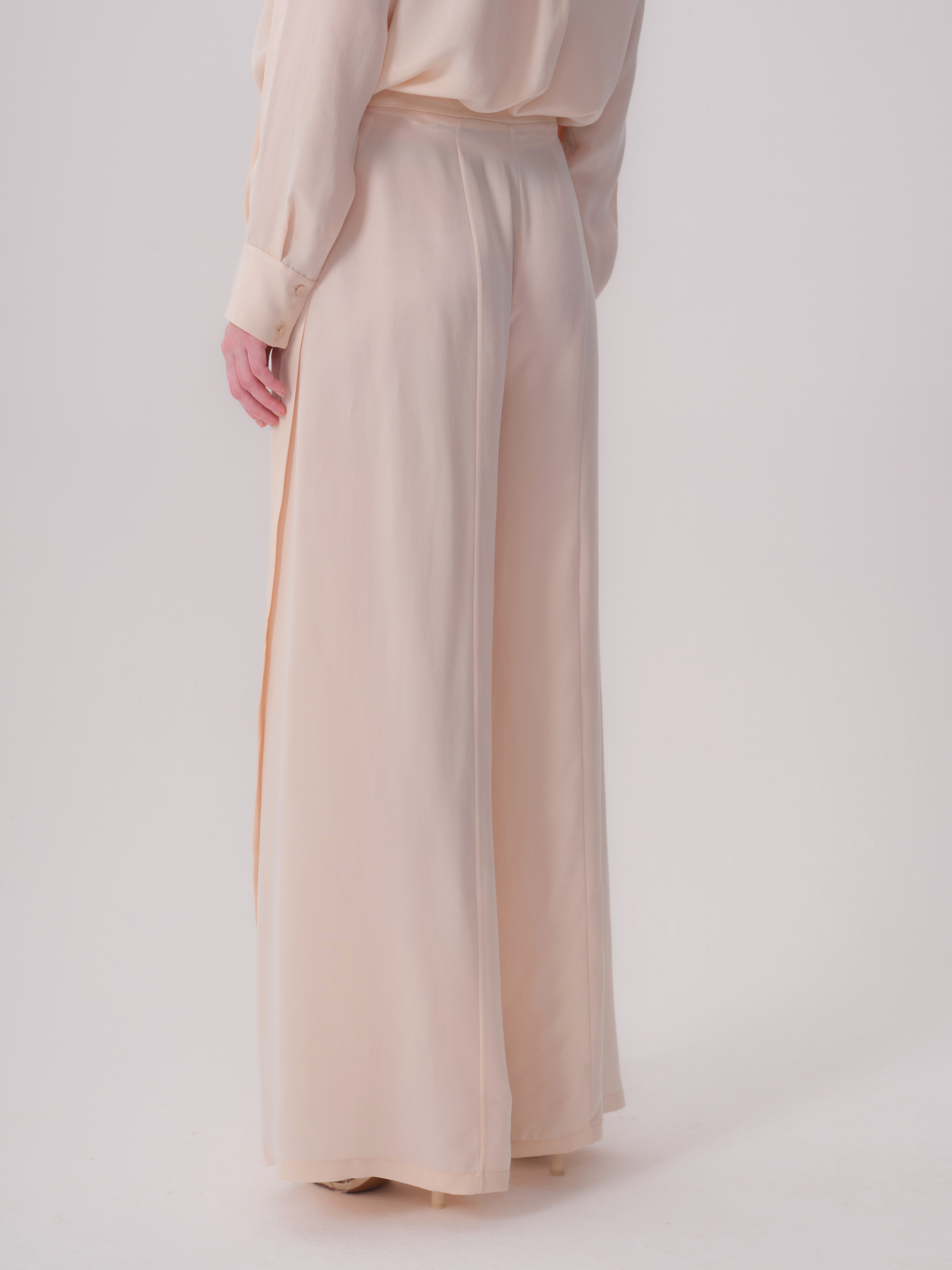 Beige wide-leg trousers with a flowing drape and a long side slit on the left leg.