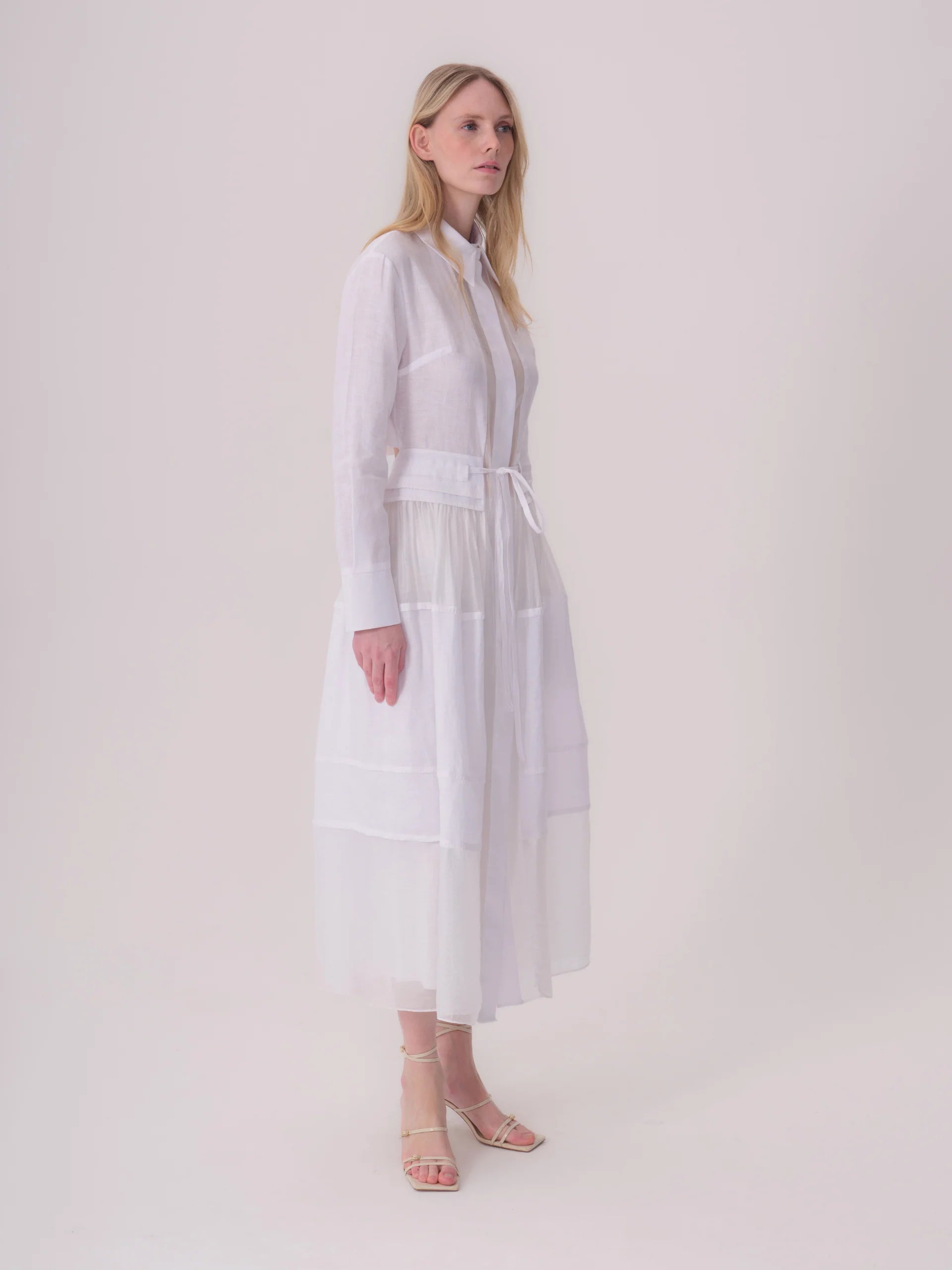 White long-sleeved shirt dress with a collar, button-front placket, drawstring waist, and a tiered, semi-sheer skirt.