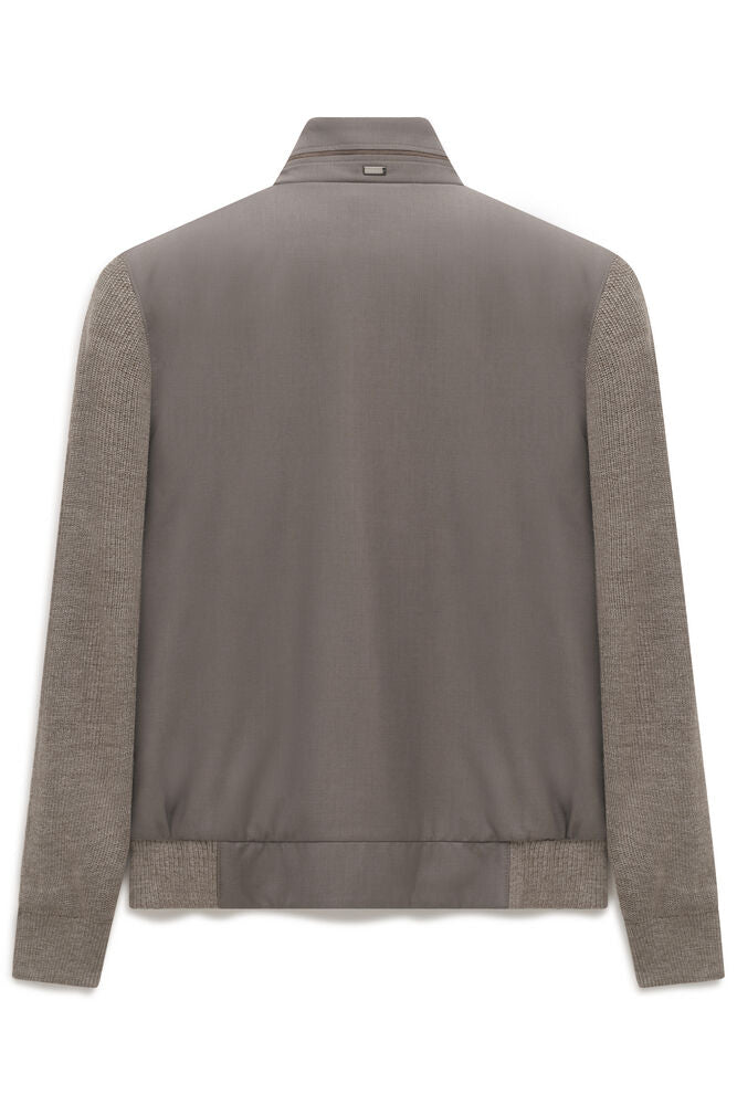 Back of a beige cardigan with a smooth body and knit sleeves. Features a stand collar with a zipper and a small gold-toned de