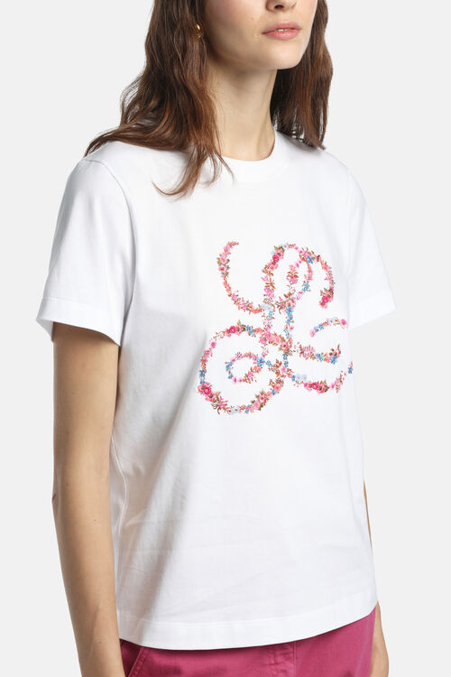 Off-white short-sleeved t-shirt with a crew neck. Features a large, intricate floral monogram on the front in pink, blue, and