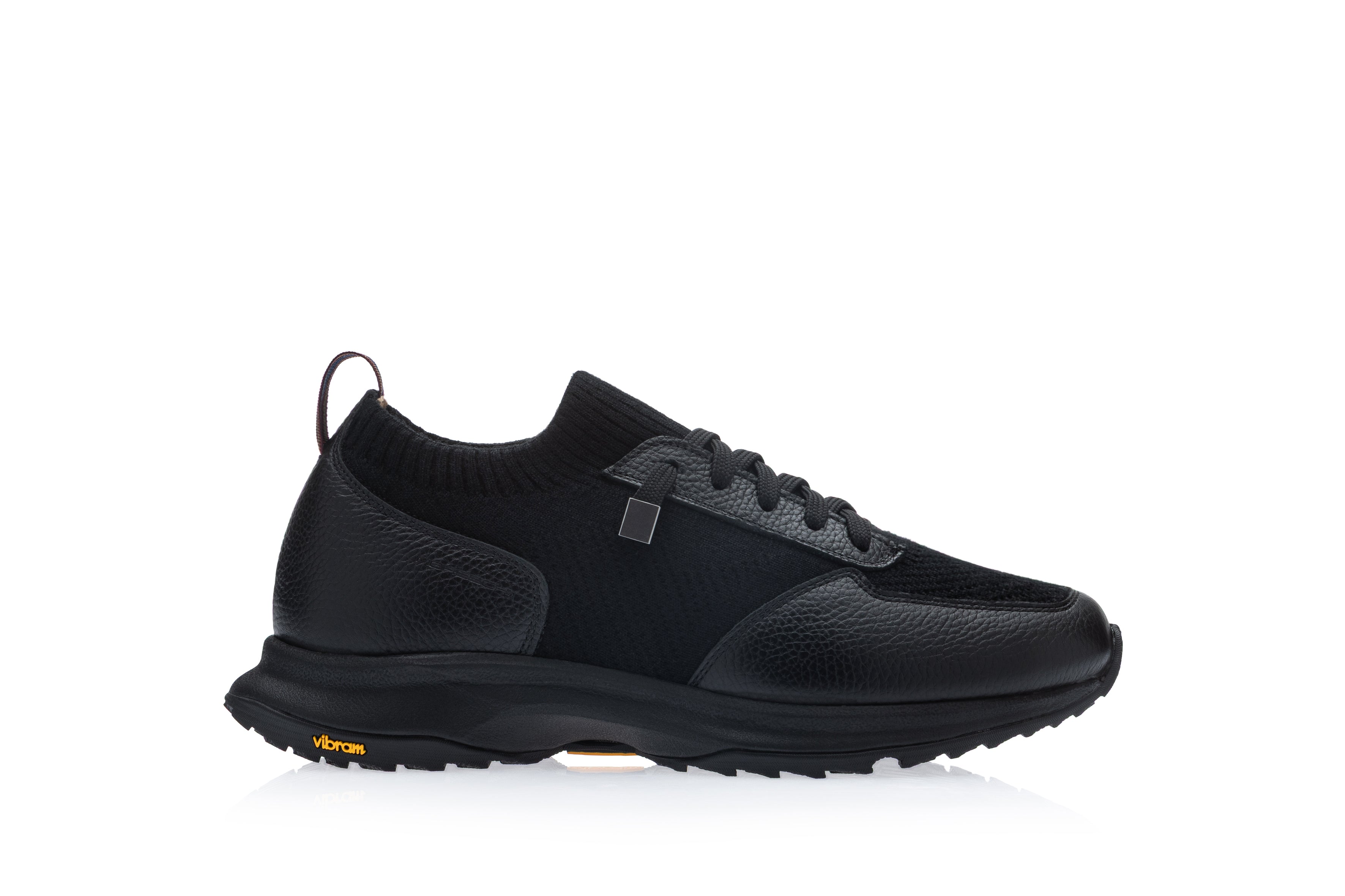 Black low-top sneaker with pebbled leather and knit panels, black laces, silver-toned detail, back pull tab, and a black Vibr