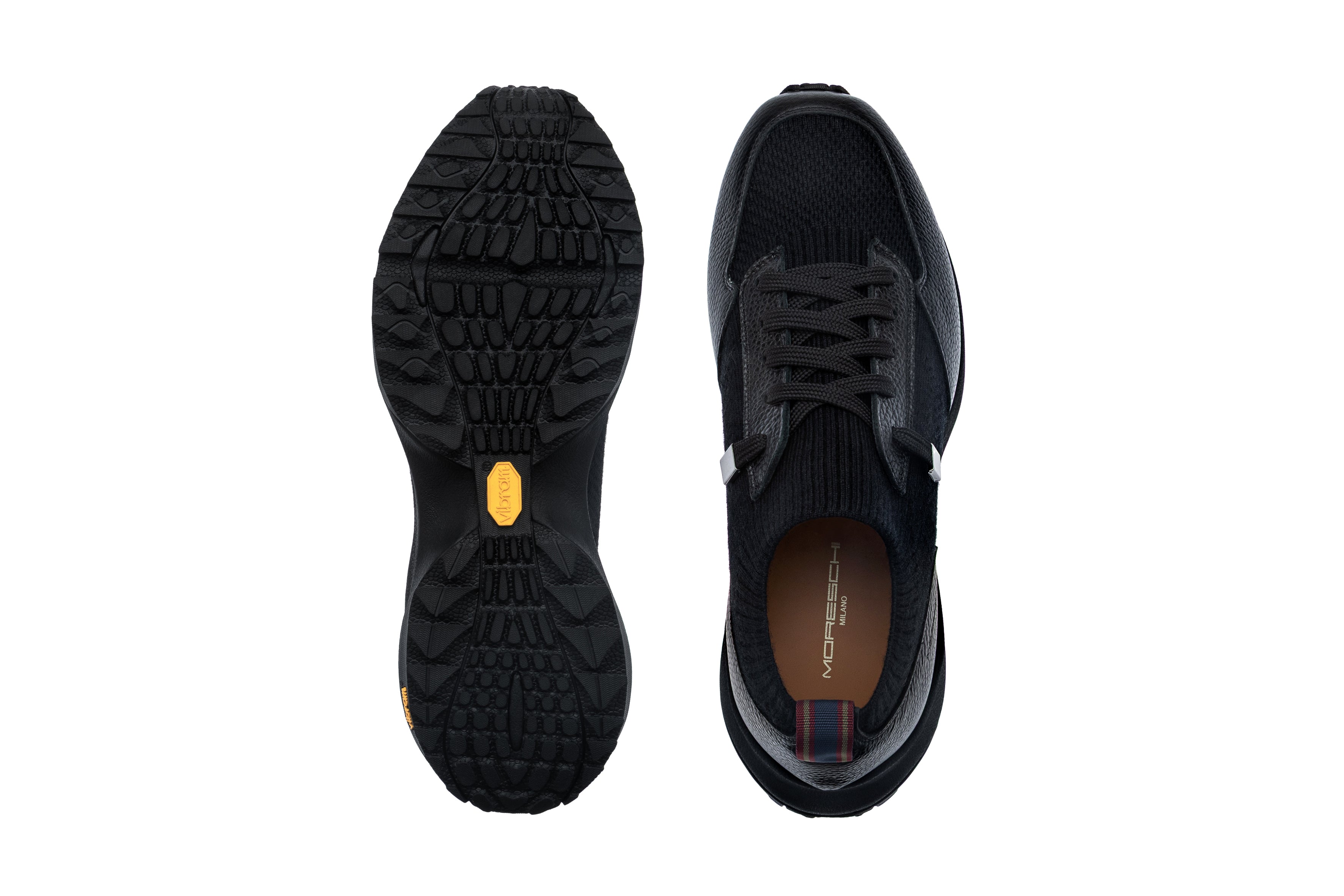 Black sneaker with knitted upper, pebbled overlays, flat laces, and a striped heel tab. Black rubber sole with aggressive tre
