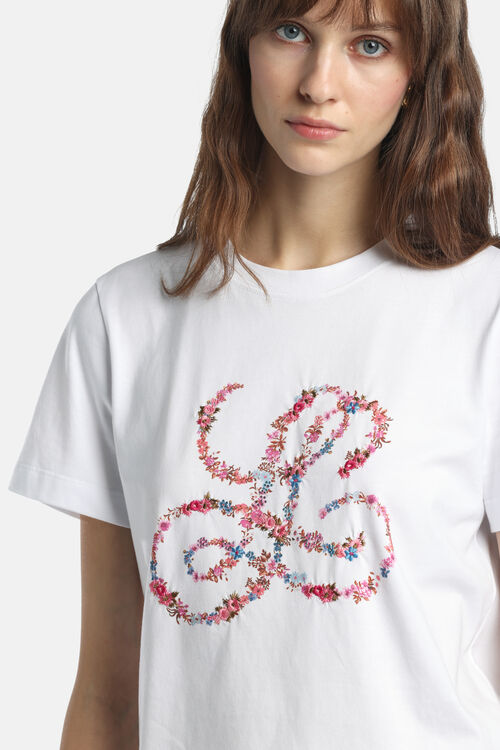 Off-white short-sleeved t-shirt with a crew neck. Features a large embroidered floral monogram in pink, blue, and green on th