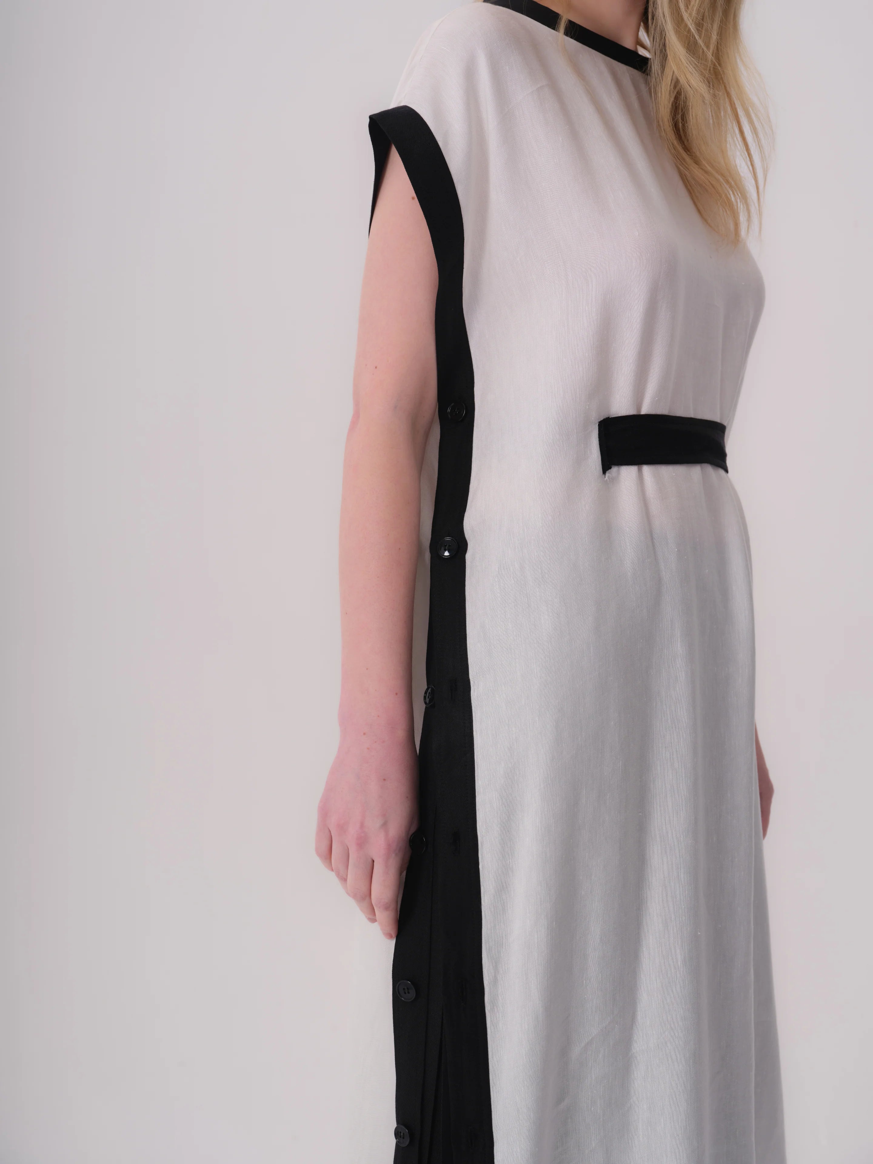 White sleeveless dress with black trim on round neck and armholes. Features a black horizontal band and a vertical black butt