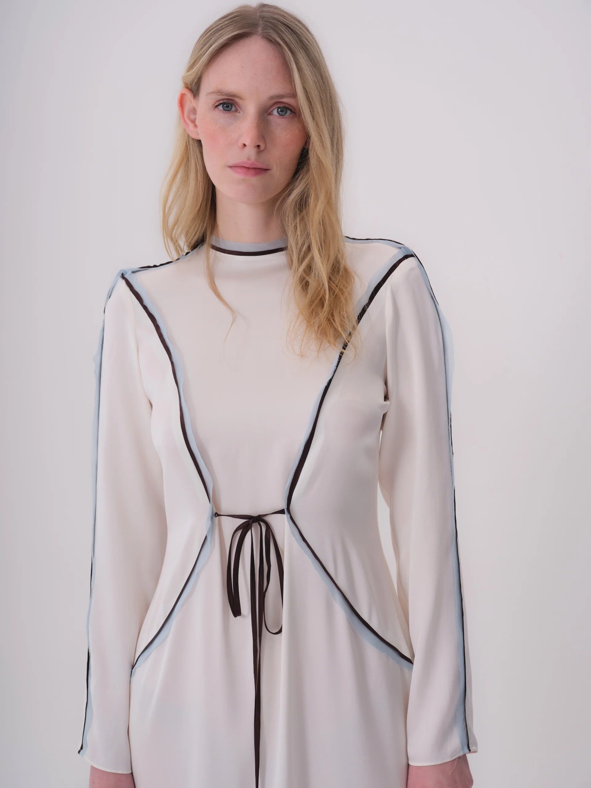 Ecru long-sleeved dress with mock neck, brown and light blue piping, and a brown ribbon waist tie.