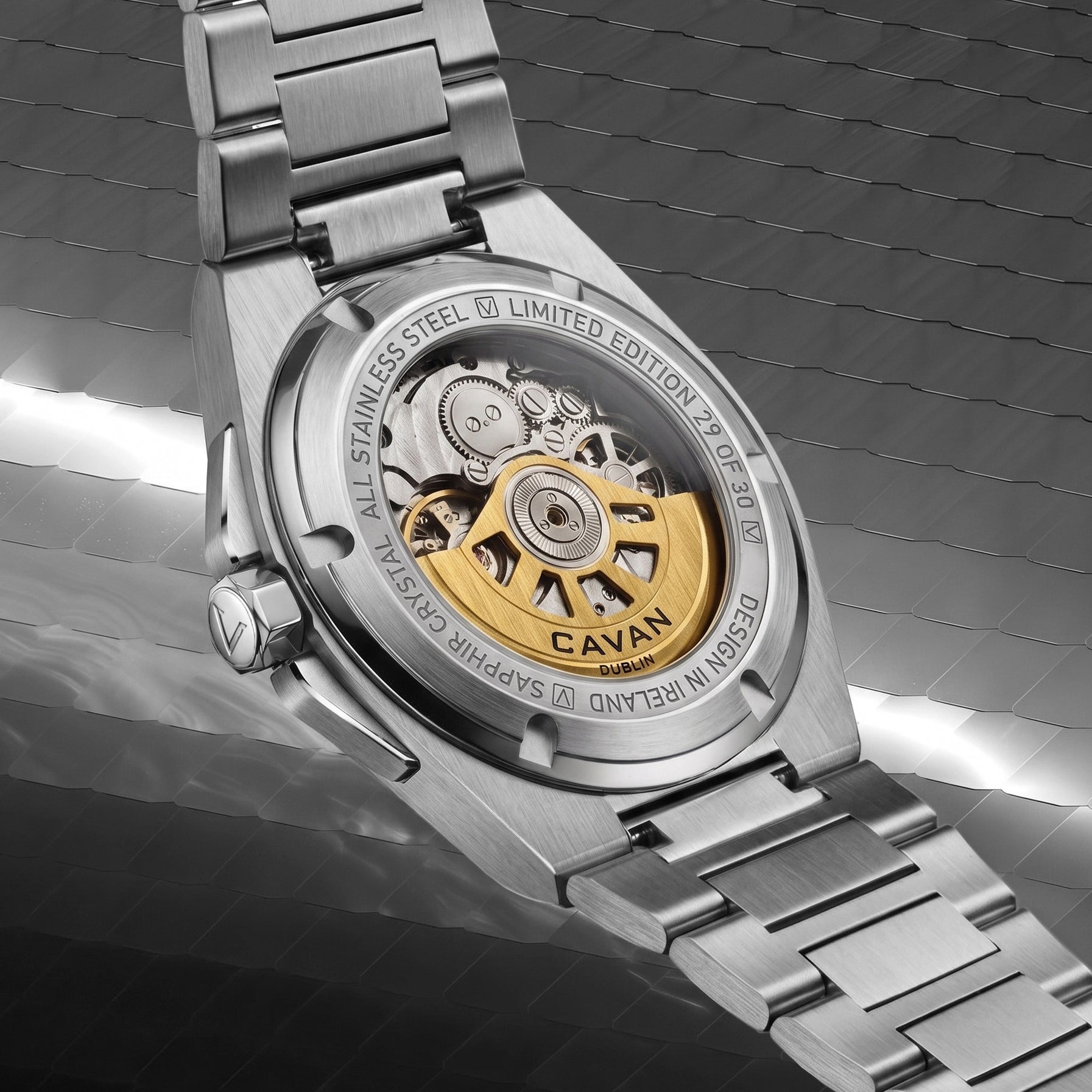 Silver-toned watch, back view. Clear case back reveals internal gears and a gold-toned "CAVAN DUBLIN" rotor. Stainless steel