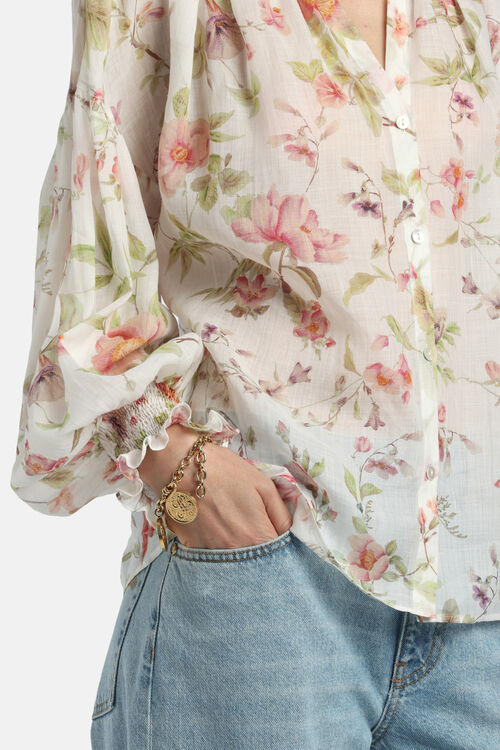Off-white floral blouse with pink and green flowers, a V-neck, and long sleeves with smocked, ruffled cuffs.