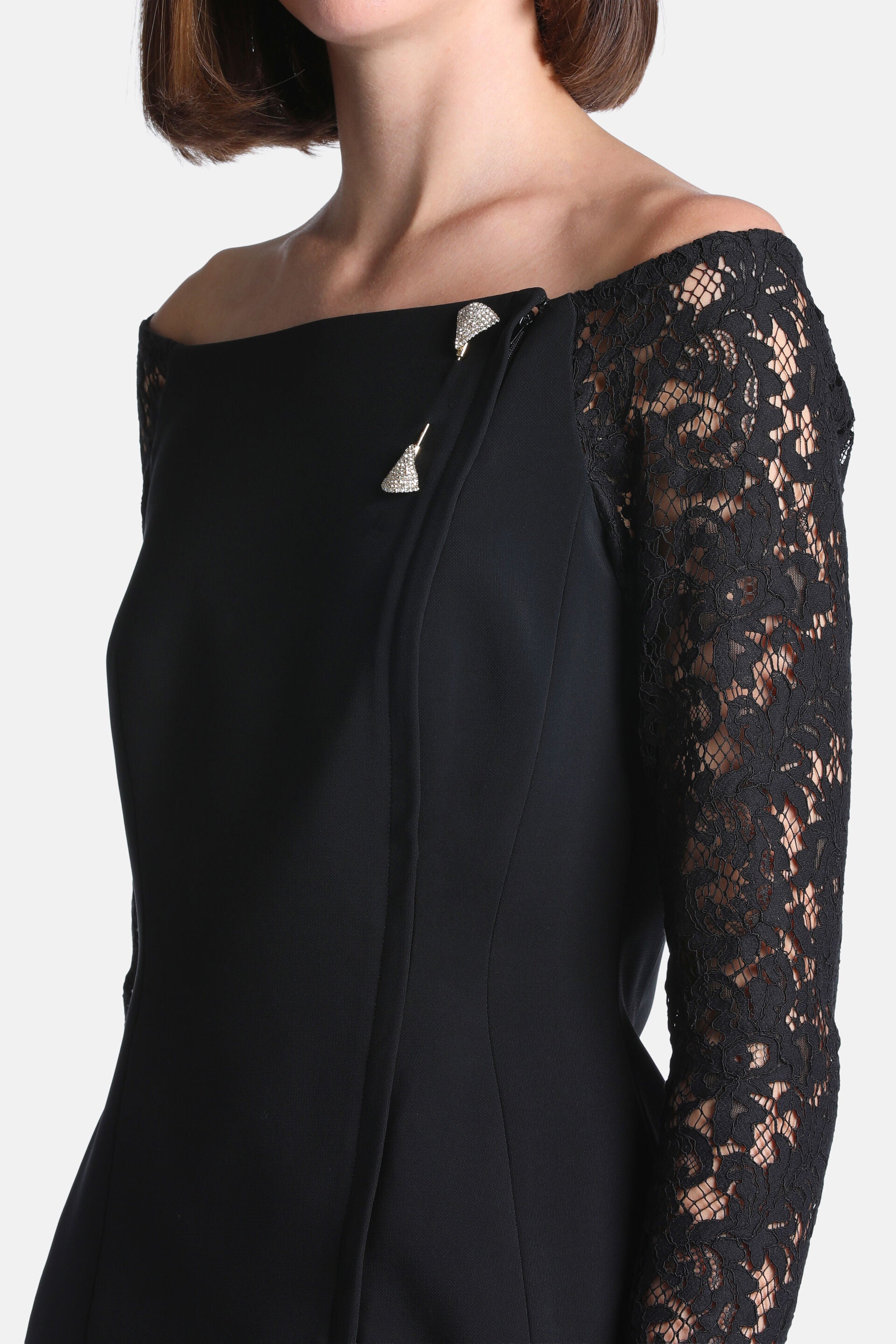 Black off-the-shoulder jacket with a lace right sleeve and solid left side. Two bell-shaped, silver-toned rhinestone pins sec