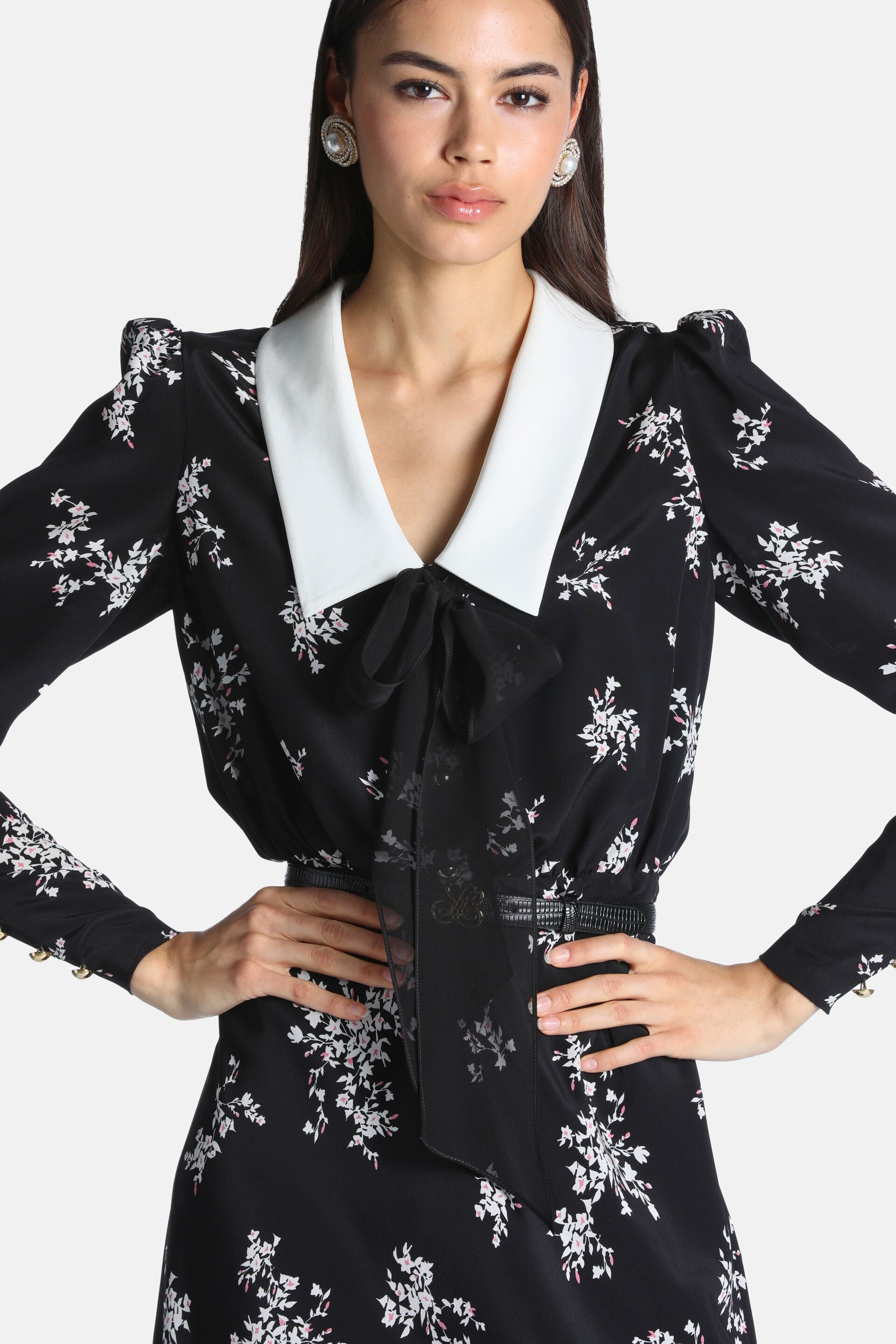 Black floral dress with white Peter Pan collar, sheer tie-neck bow, puffed shoulders, textured belt, and gold-toned cuff butt