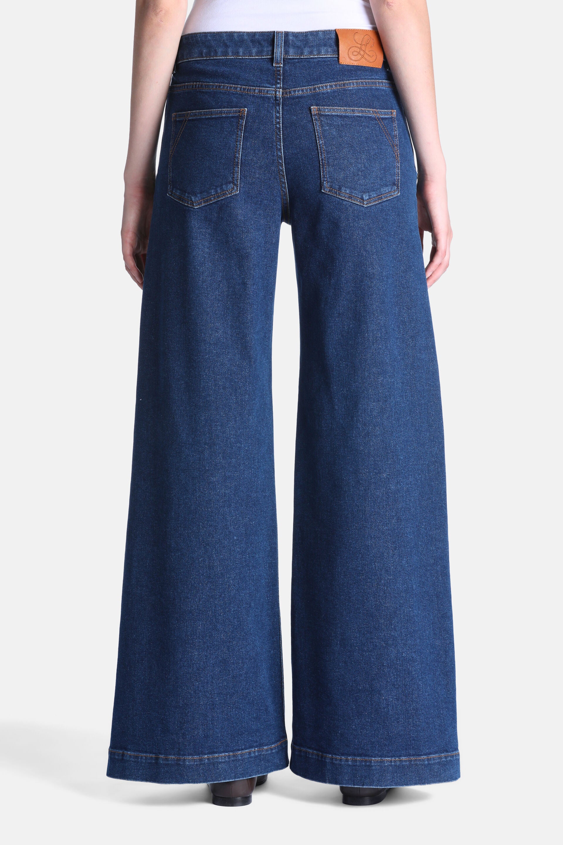 Dark blue denim wide-leg trousers with two back patch pockets, a brown leather-like logo patch on the waistband, and contrast