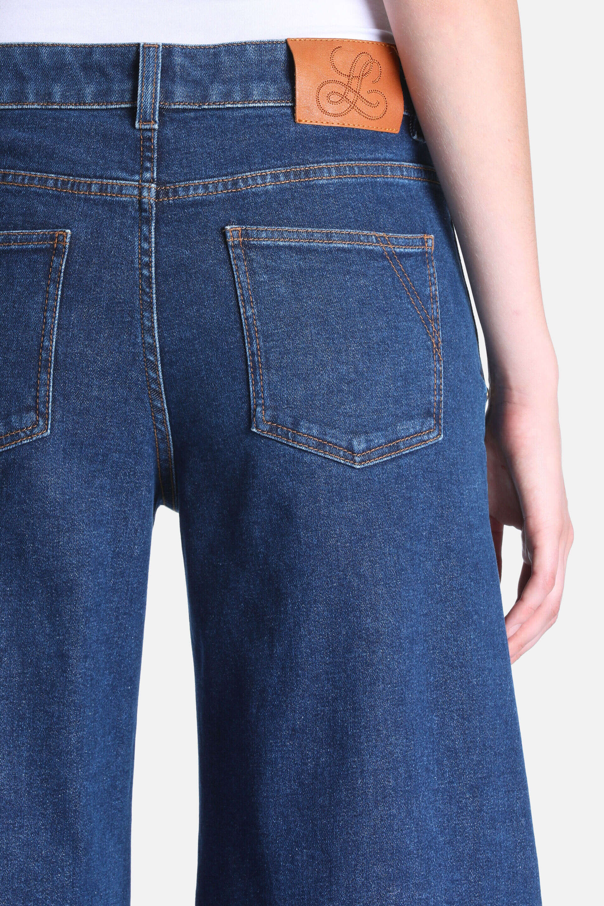 Dark blue denim trousers, back view. Two back pockets with triangular stitching, orange-brown seams, brown leather logo patch