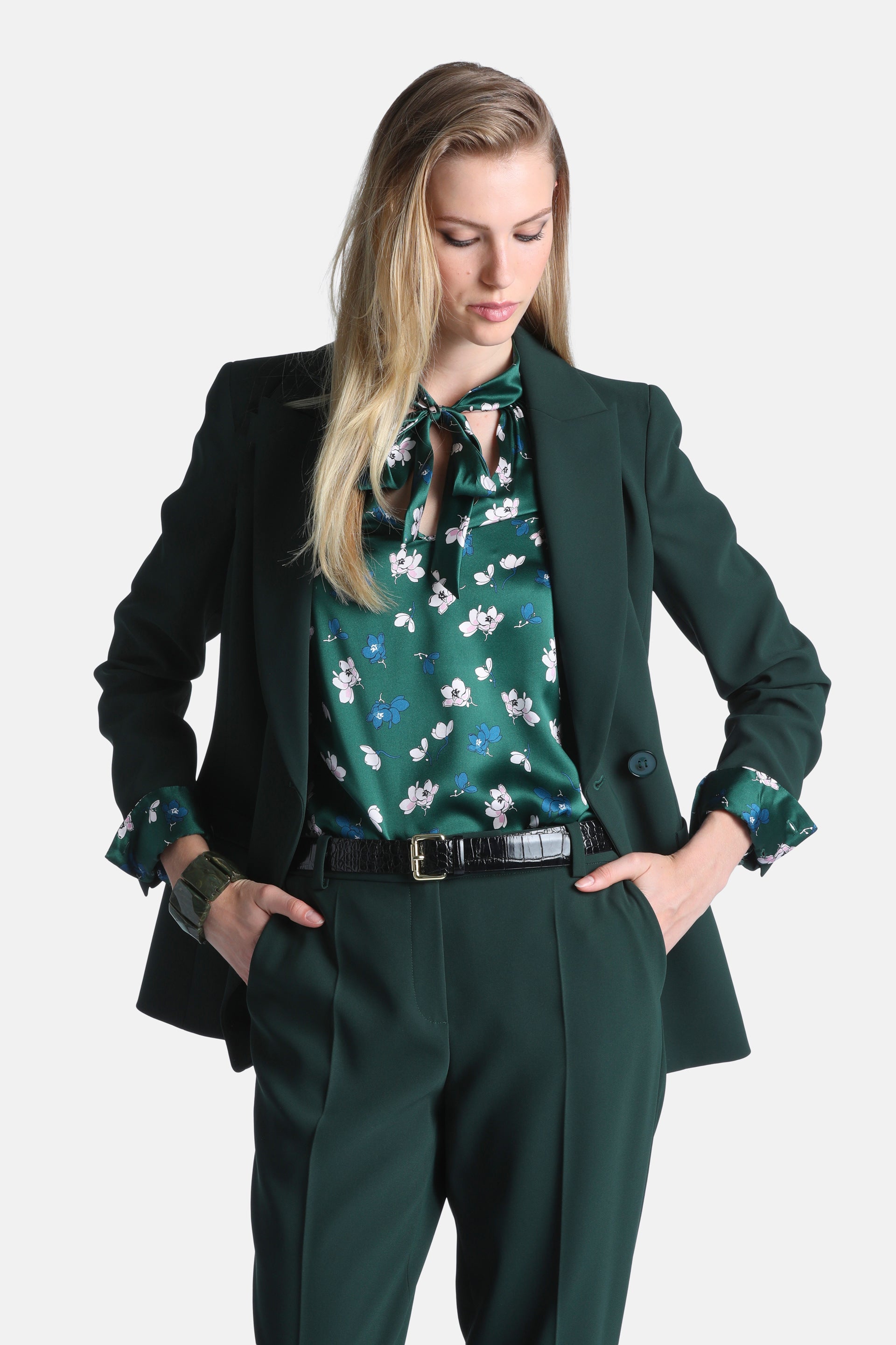 Dark green blazer with notched lapels and a single button closure. The long sleeves are cuffed, revealing a floral lining.