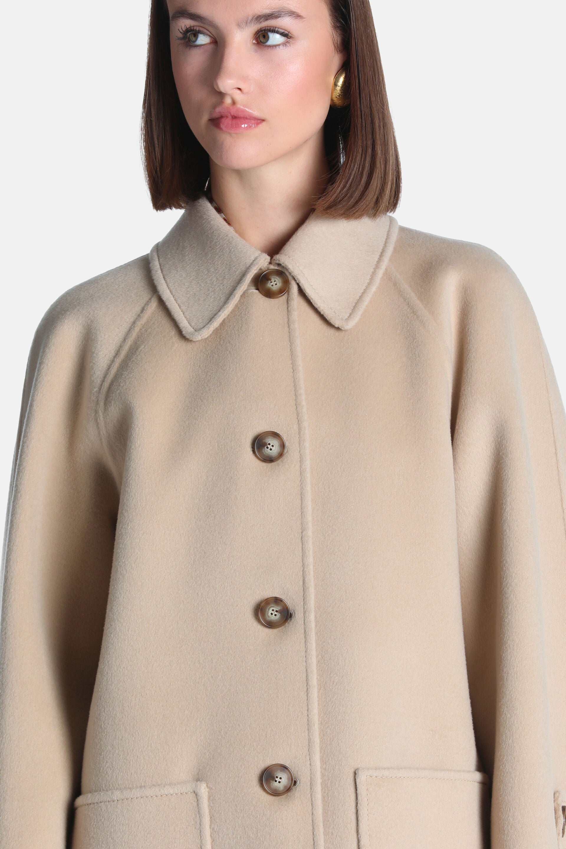 Camel wool coat with a pointed collar, raglan sleeves, four brown buttons down the front, and two visible patch pockets.